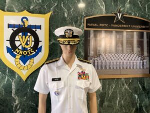 Display at Vanderbilt Navy ROTC unit, including the unit crest, a photo of current midshipmen, and a mannequin wearing a summer white uniform with two star admiral insignia, aviator wings, and a nametag for "YOU"
